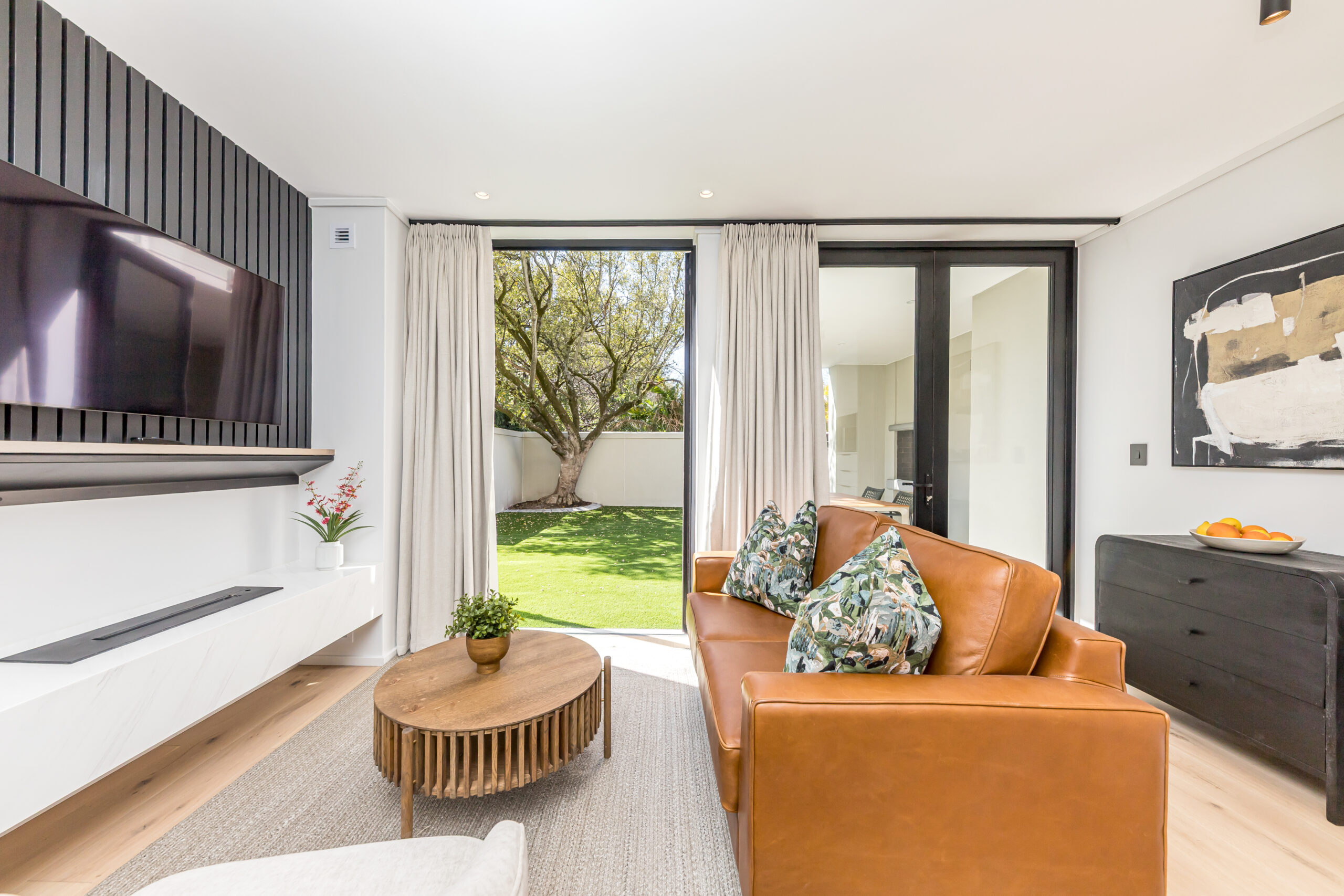 Lounge with a tan leather sofa opening onto the private lawn in the superior one apartment at Aan de Meul