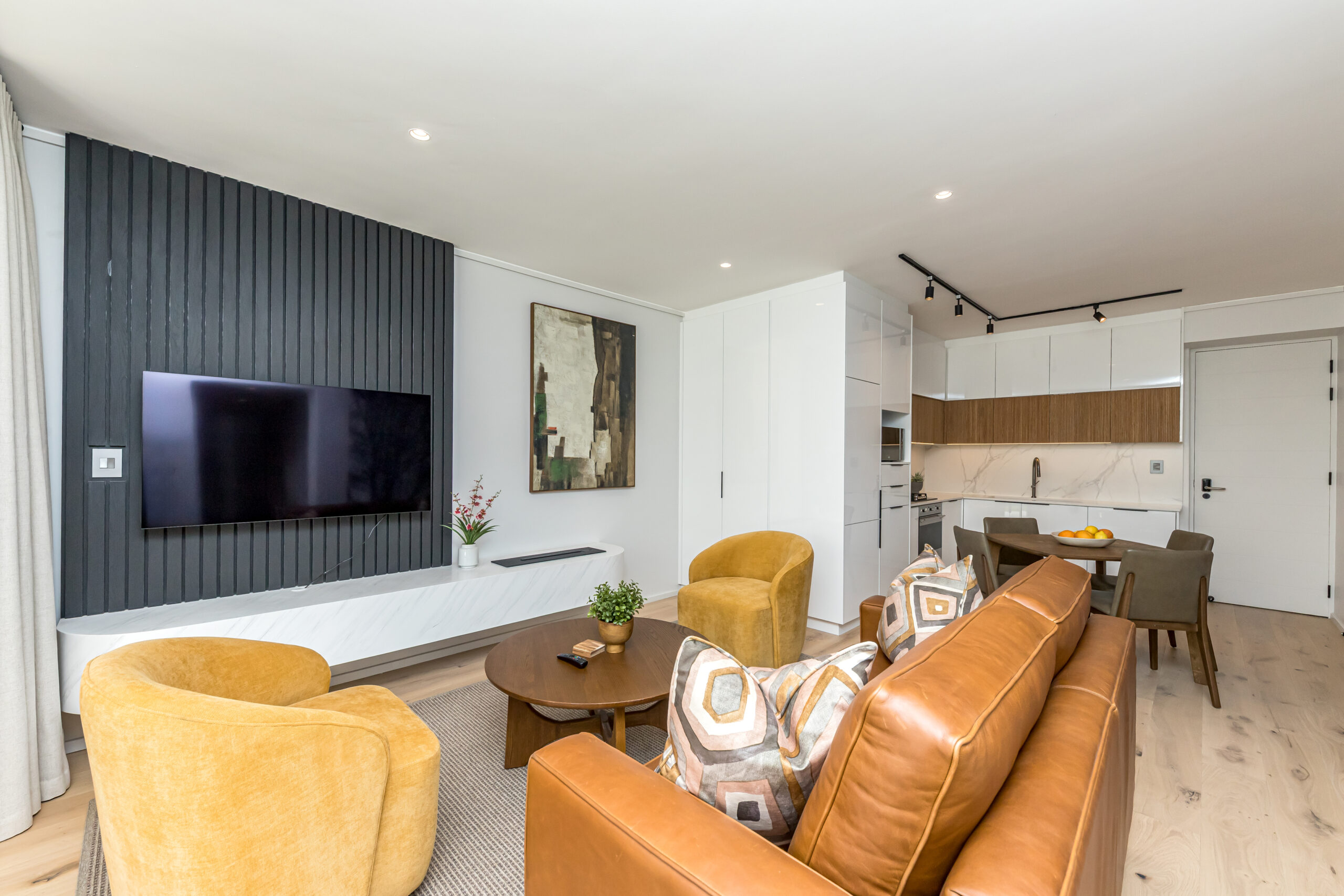 Open-plan lounge with a tan leather sofa, yellow armchairs and adjoining dining area in the superior two apartment at Aan de Meul