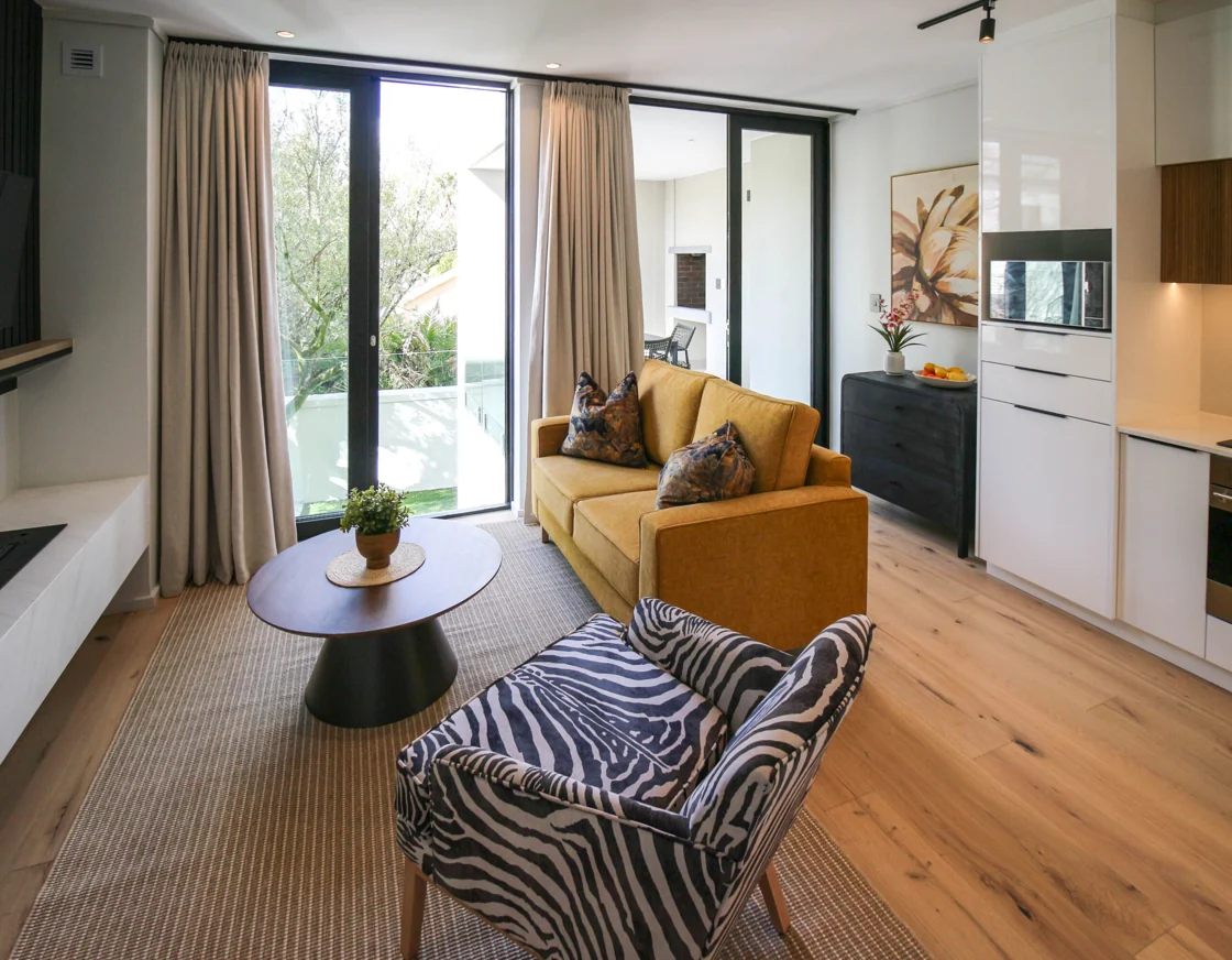 Lounge with a yellow sofa and patterned armchair beside the balcony doors in the Luxury One Bedroom apartment at Aan de Meul